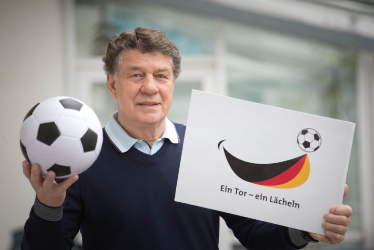 Otto Rehhagel mit Ball und Plakat "Ein Tor - ein Lächeln" in den Händen